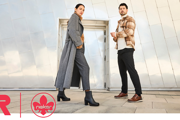 Frau in grauem Mantel und Mann in kariertem Hemd präsentieren Schuhe vor modernem Gebäude.